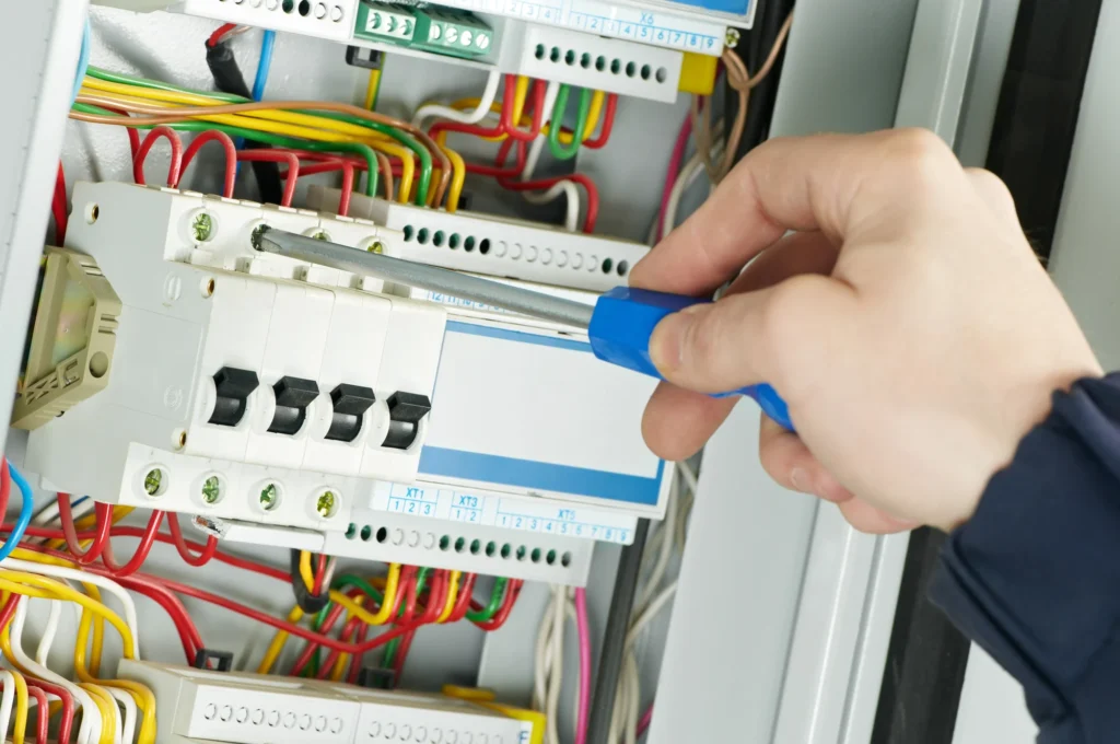 Electrician checking circuit breakers inside a switchboard with a screwdriver